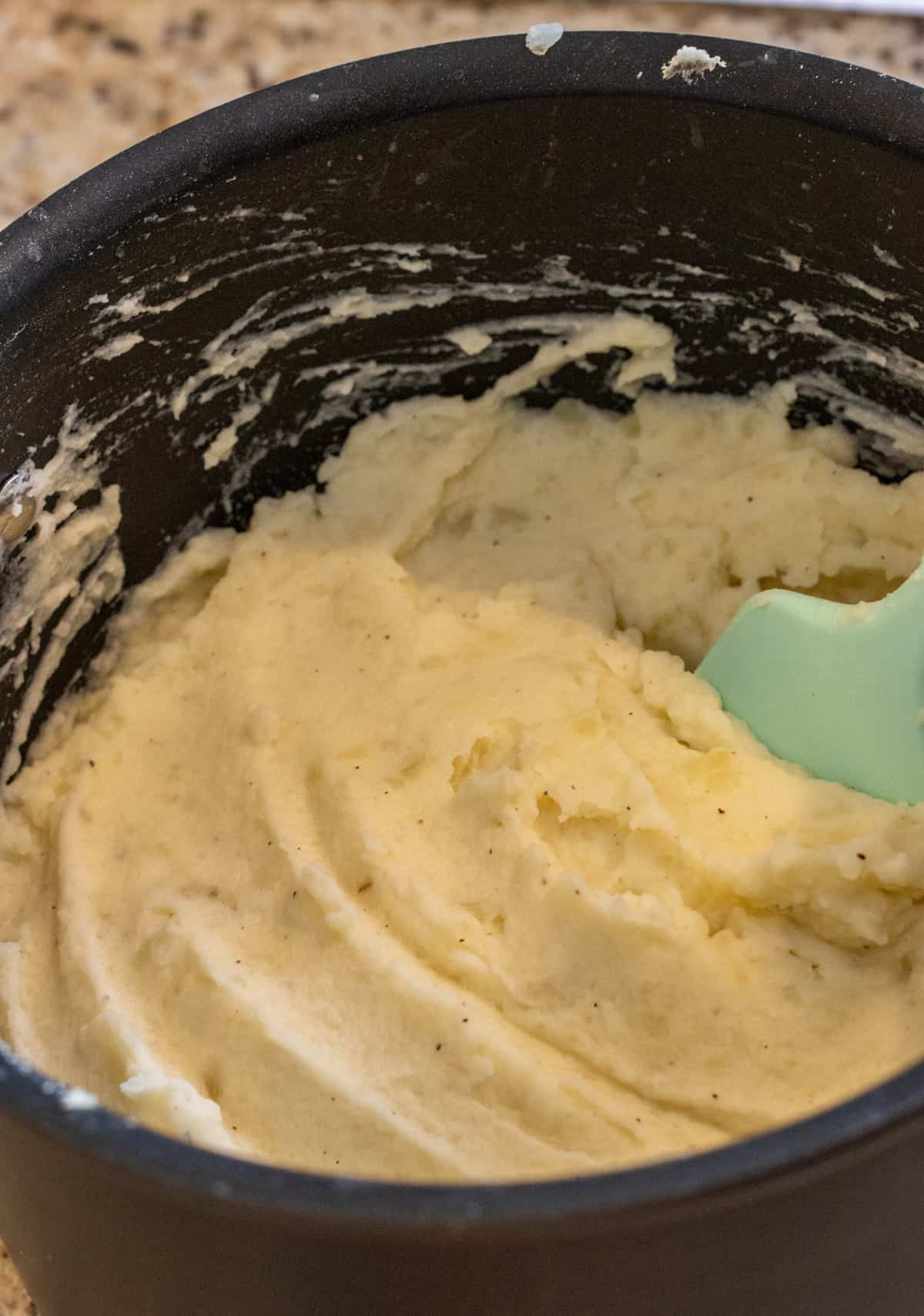 Mashed potatoes in a pot with a blue rubber spatula.