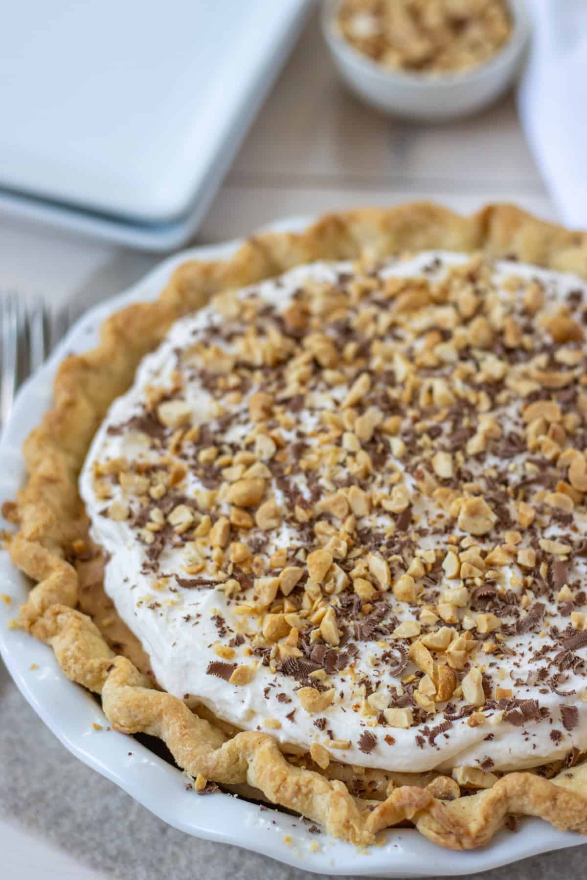 Peanut butter pie in a pie plate with plates and a bowl of peanuts in the background.
