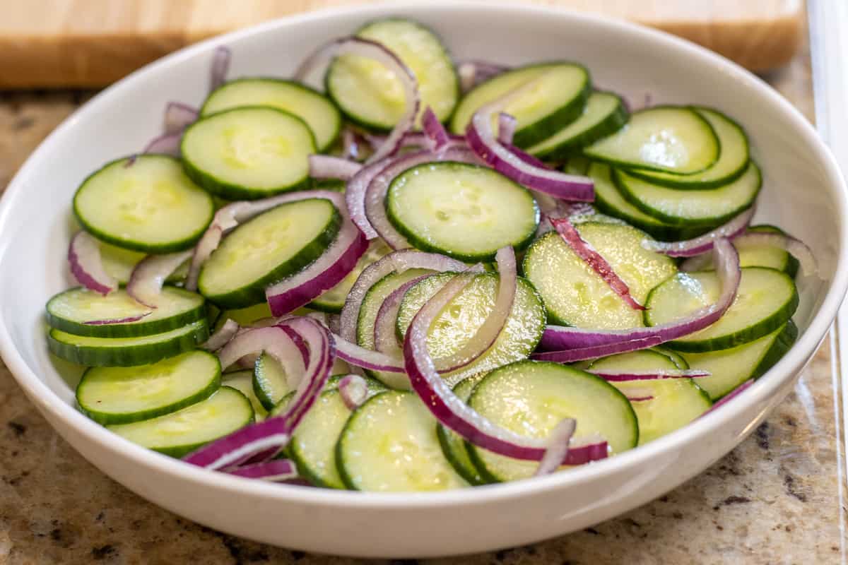 Sliced cucumbers and red onions in a bowl with apple cider vinegar.