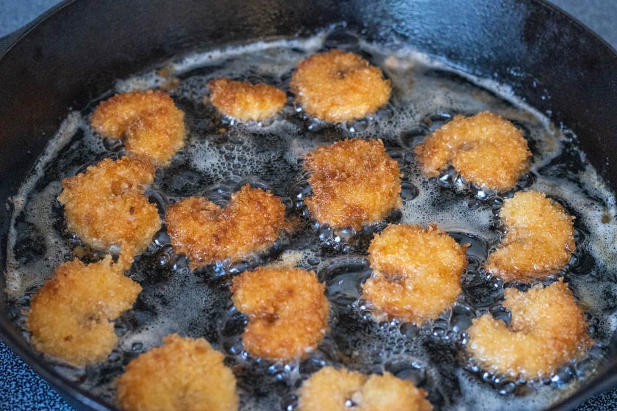 Breaded shrimp frying in a cast iron pan.