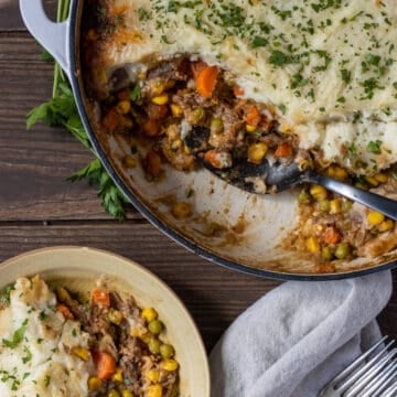 Overhead shot of shepherd's pie with a scoop taken out and on a plate with forks and a napkin next to it.