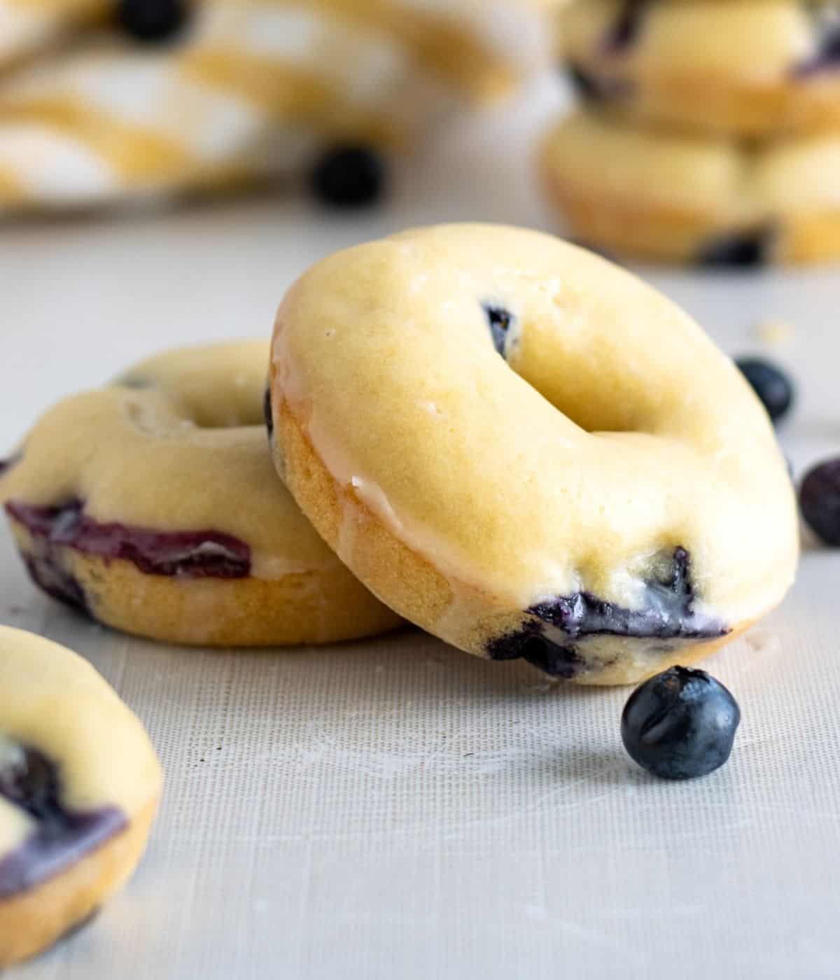 Up close shot of two blueberry donuts with loose blueberries and more donuts up front and in the background.