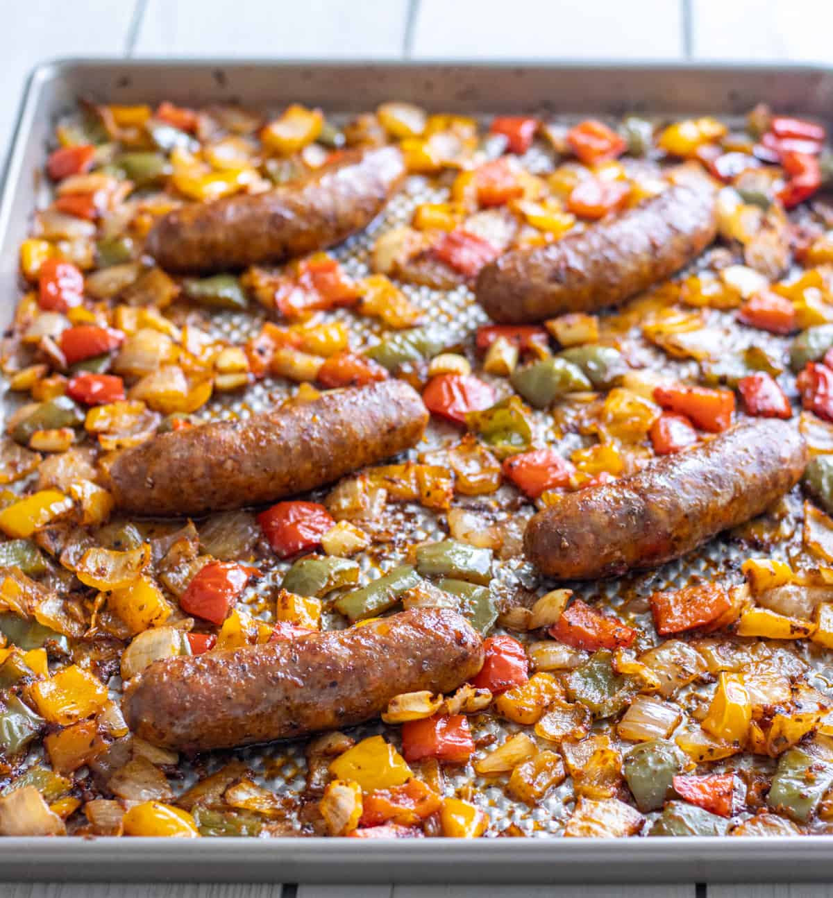 Italian sausages, bell peppers, and onions in a tomato sauce baked on a sheet pan.