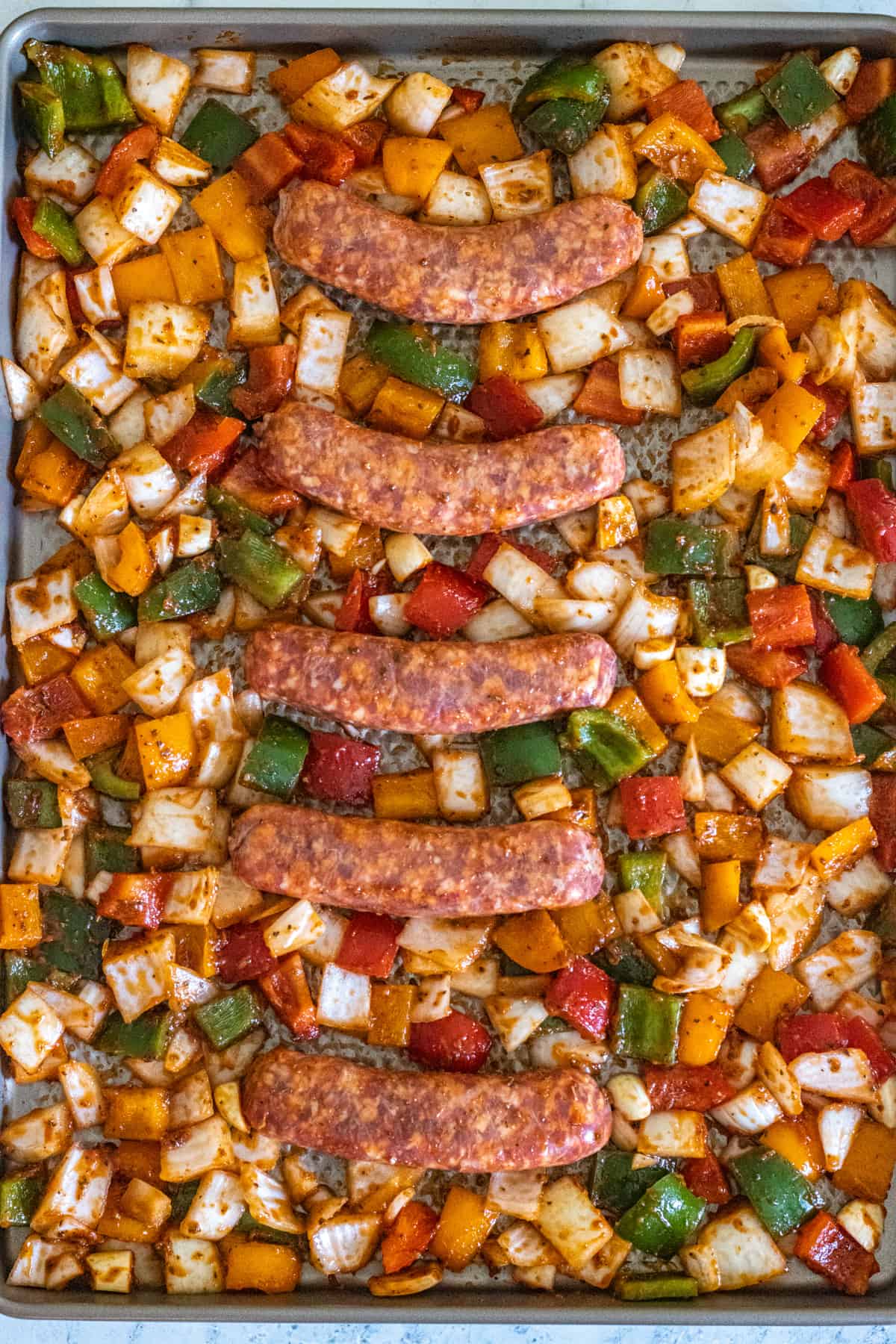 Sausages, peppers, and onions spread out on a sheet pan.