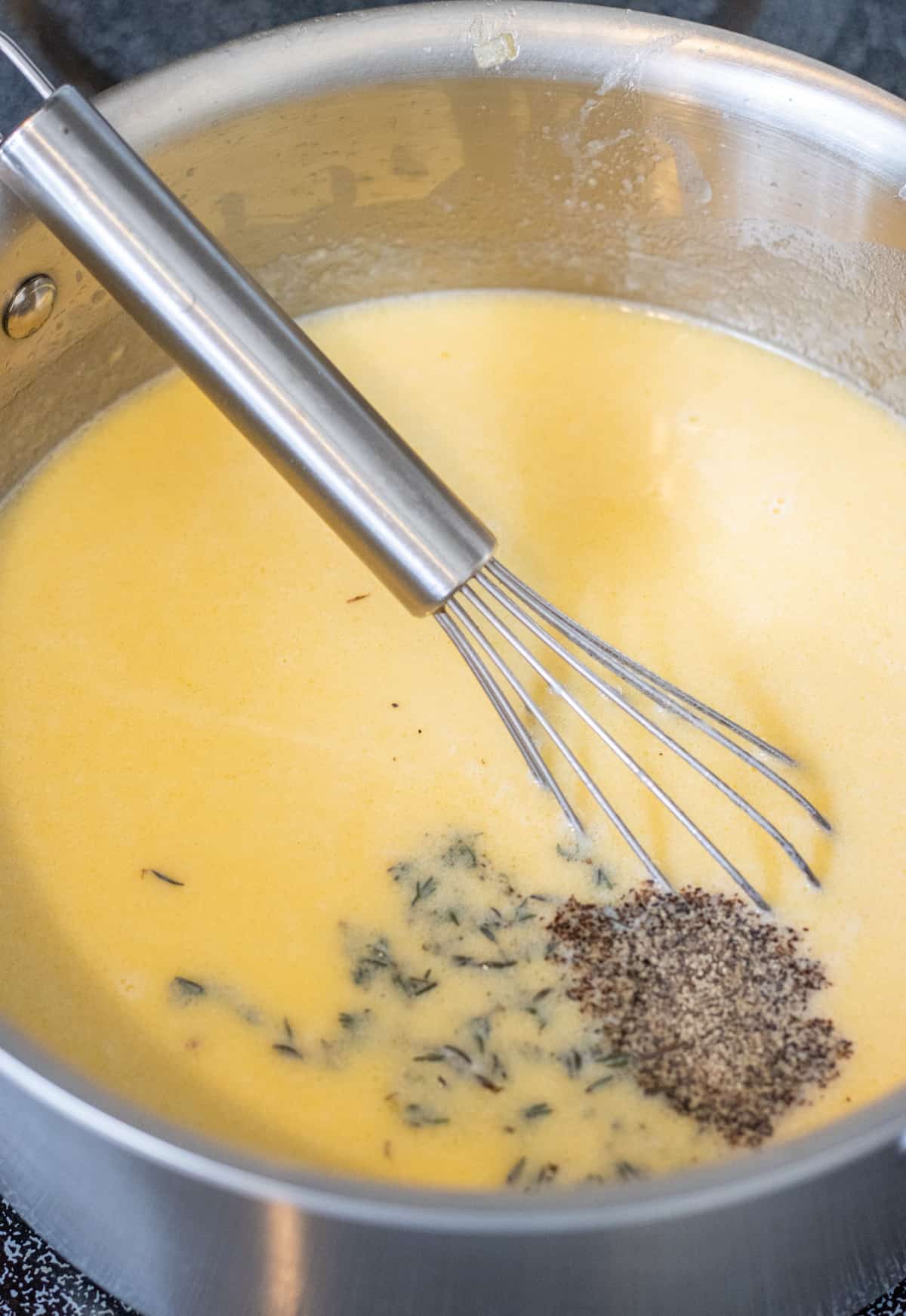 Salt, pepper, and thyme added to the cream sauce with a whisk.
