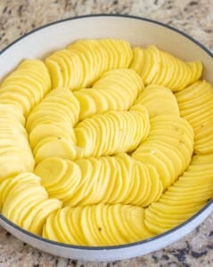 Sliced potatoes arranged in a round baking dish.