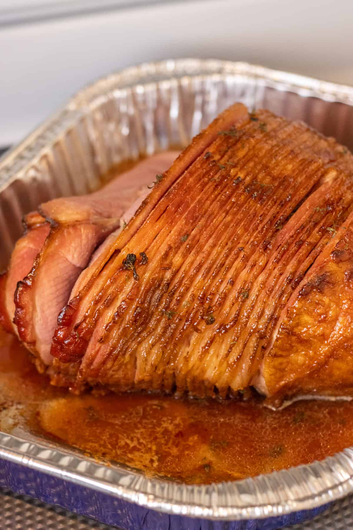 Spiral sliced honey glazed ham in a foil roasting pan with pan drippings.
