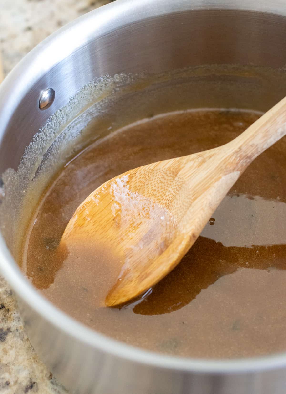 Honey brown sugar glaze in a saucepan with a wooden spoon.