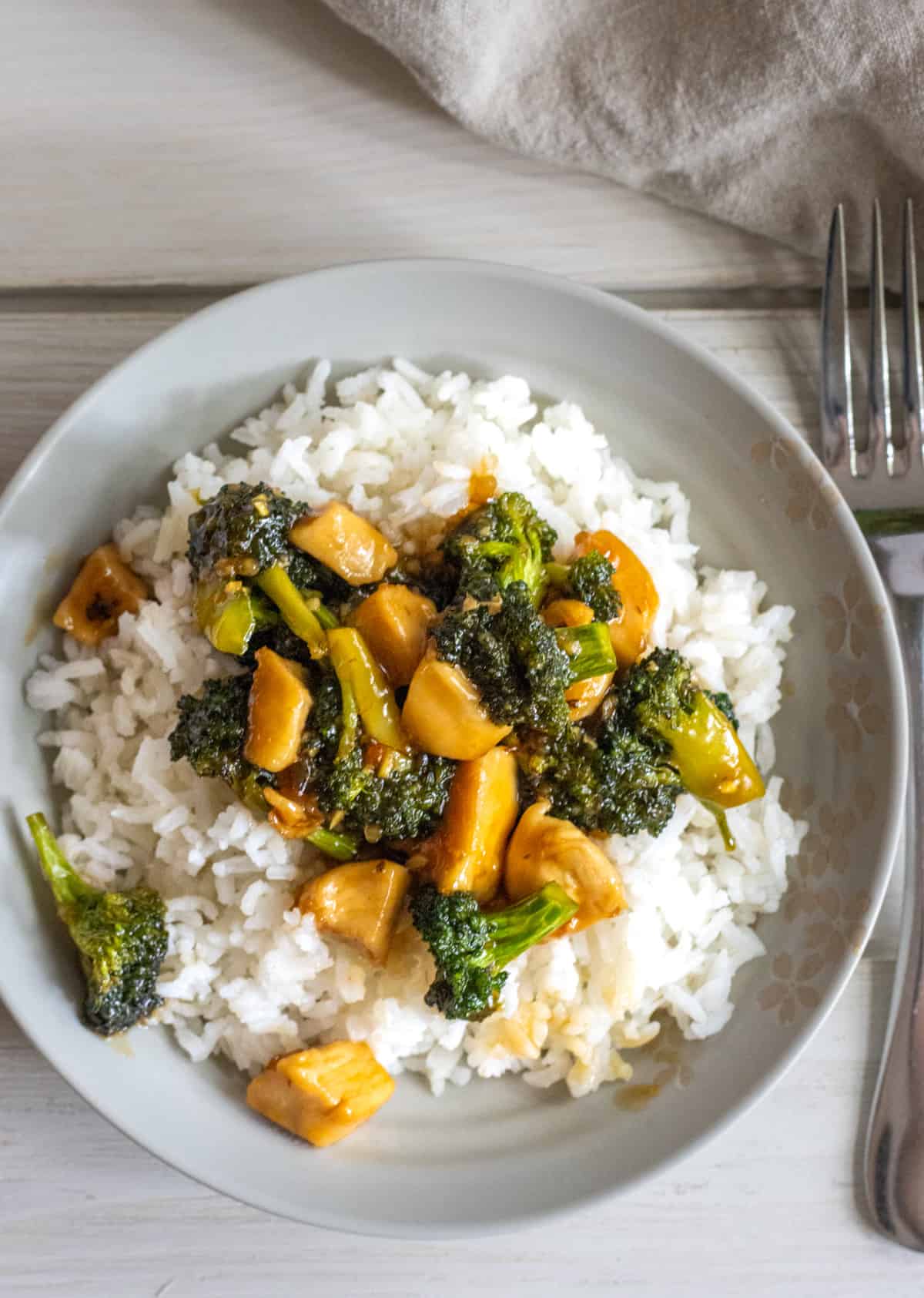 Plate of rice topped with honey garlic chicken stir fry with broccoli florets.