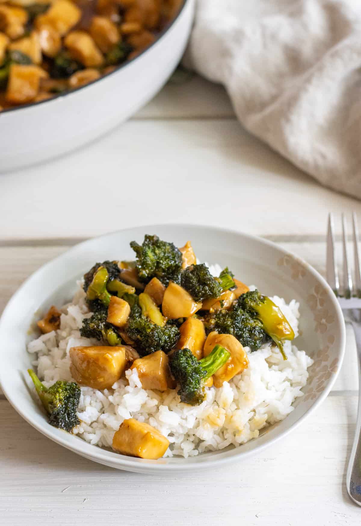 A plate of honey garlic chicken stir fry with broccoli next to the skill with the stir fry.