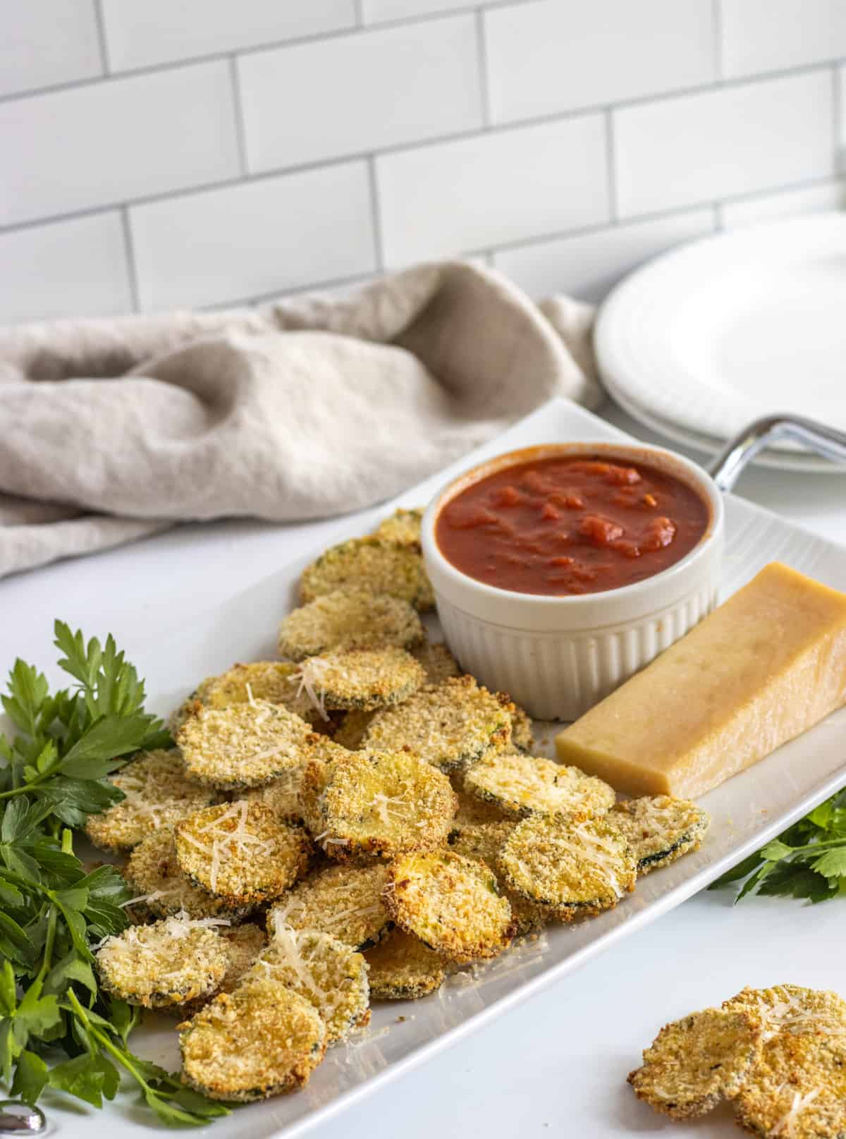 Oven fried zucchini chips on a tray with a bowl of marinara.
