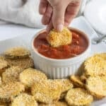 A hand dipping a breaded zucchini chip into a bowl of marinara.