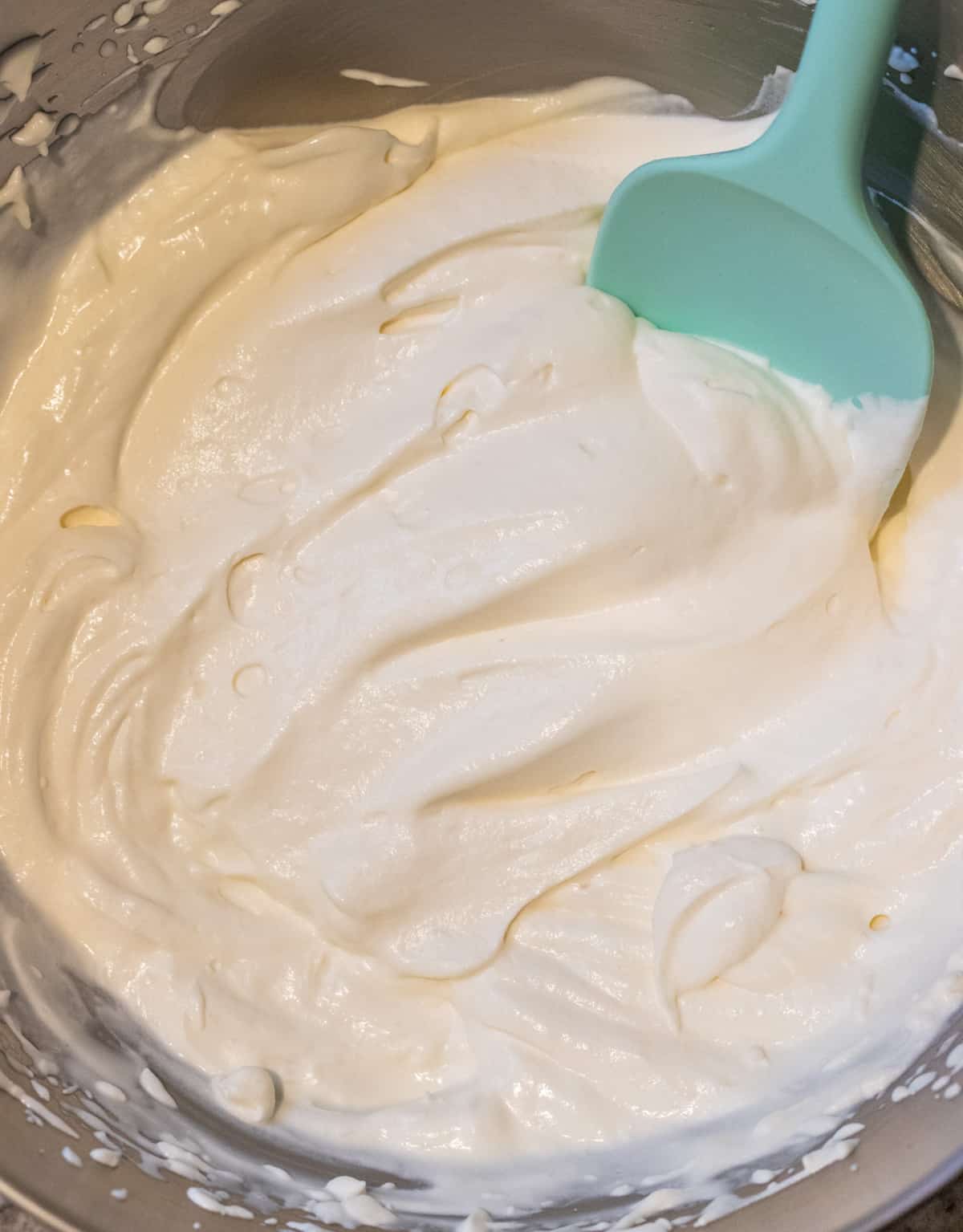 Creamy whipped topping in a bowl with a blue spatula.