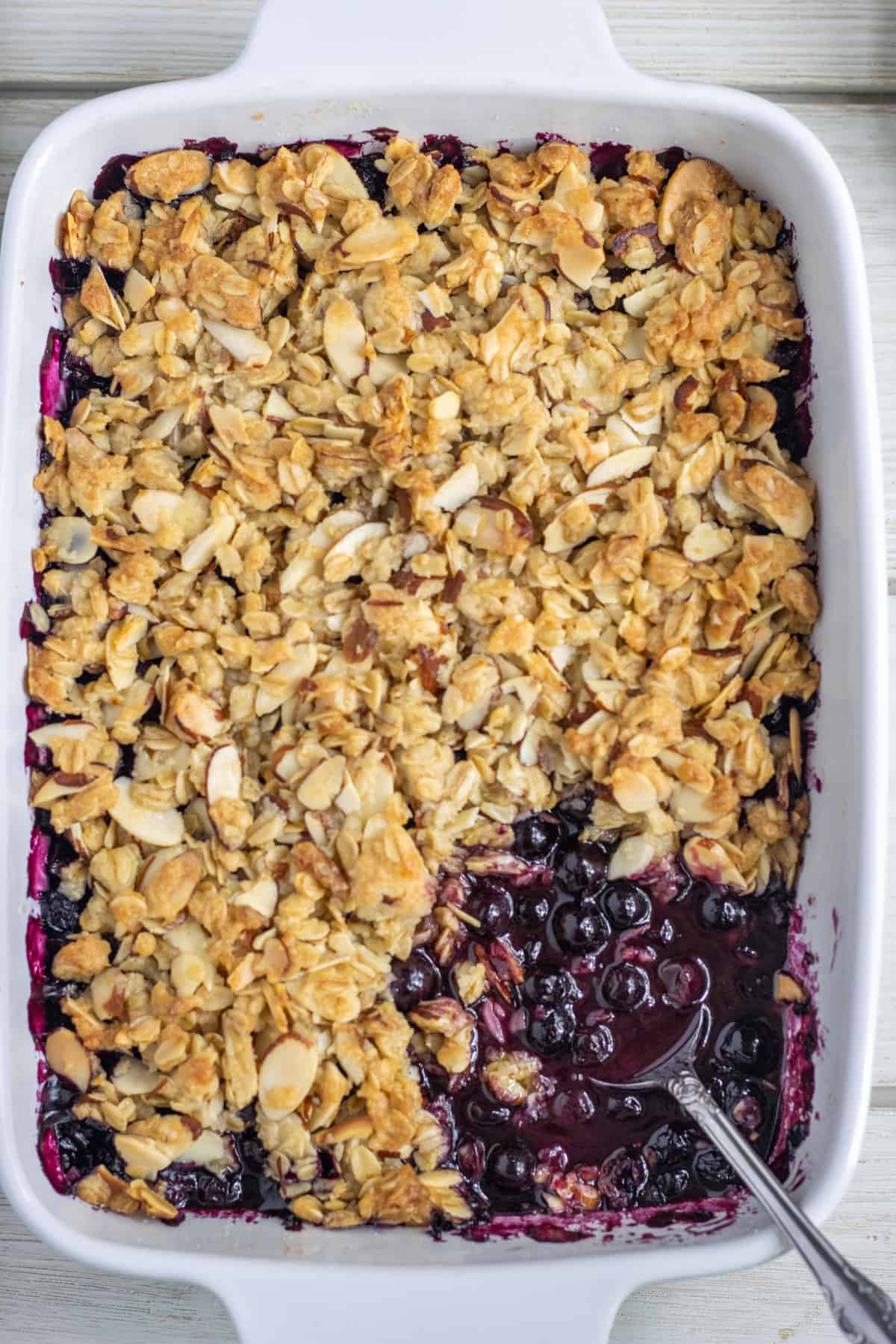 Blueberry crisp with scoop missing and a spoon.