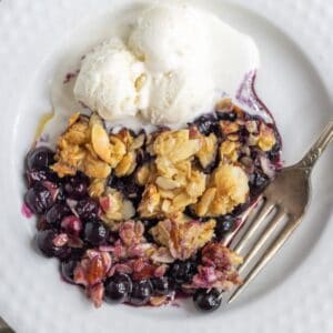 Blueberry crisp on a plate with ice cream.