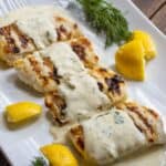 Grilled haddock filets on a platter with creamy lemon dill sauce poured over them.