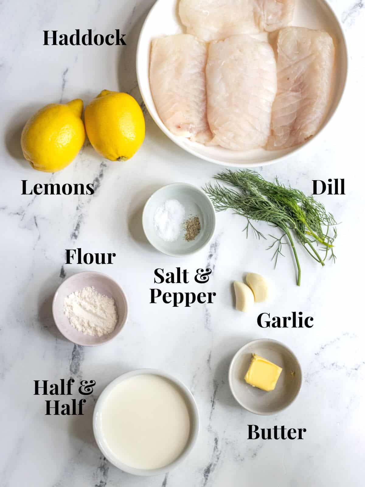 Ingredients for grilled haddock and creamy lemon dill sauce on a marble background with labels.