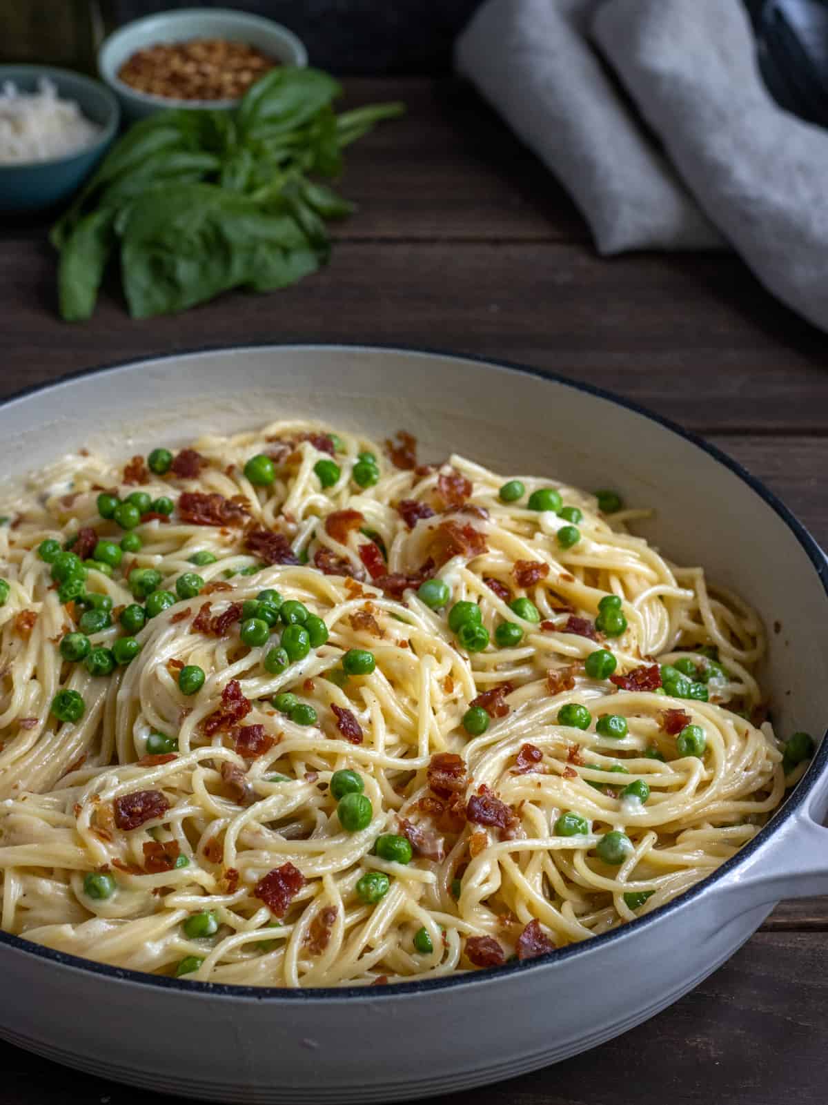 Spaghetti Alfredo with peas and prosciutto in a white casserole dish.