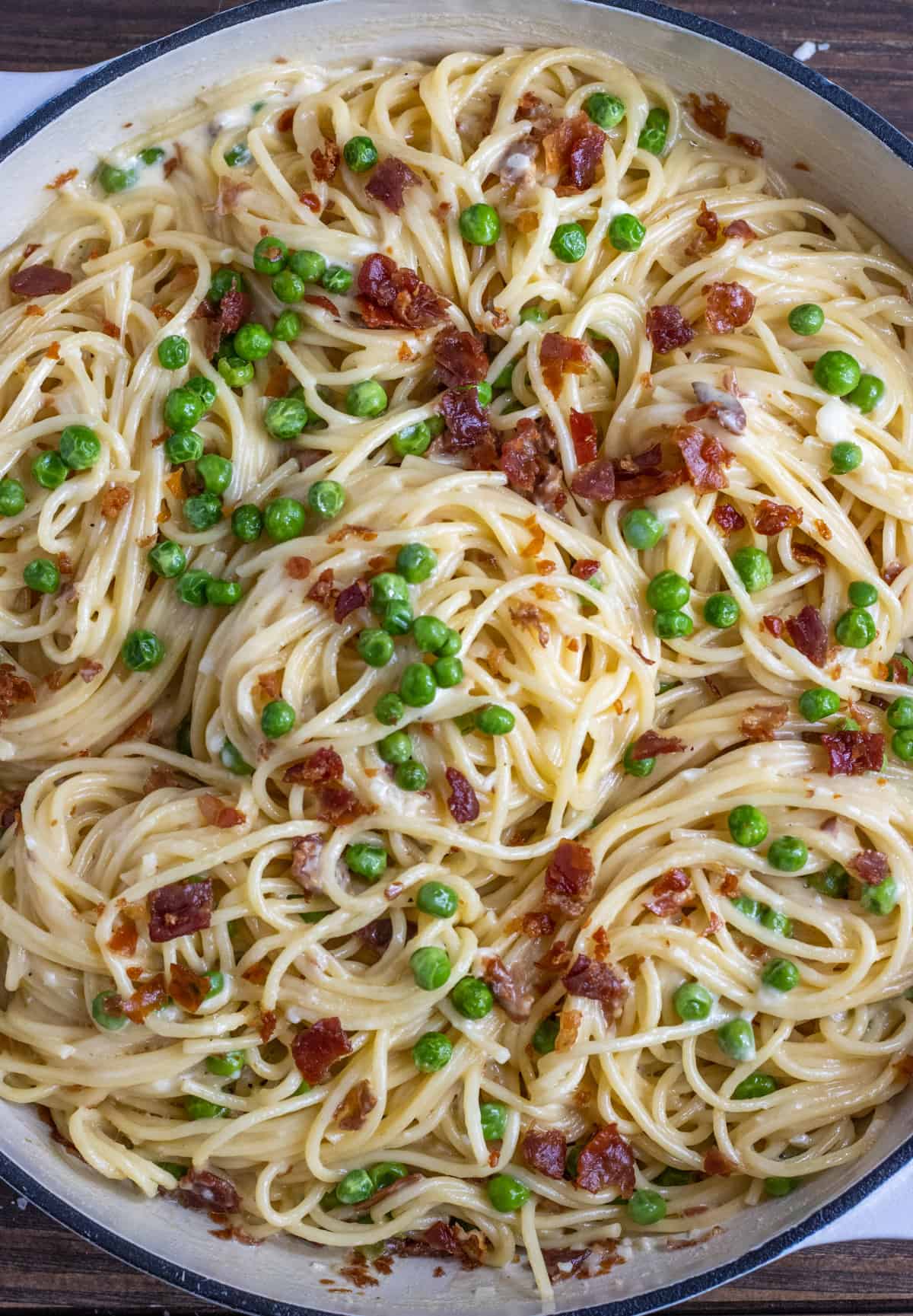Spaghetti noodles in Alfredo sauce with peas and crispy prosciutto in a white casserole dish.