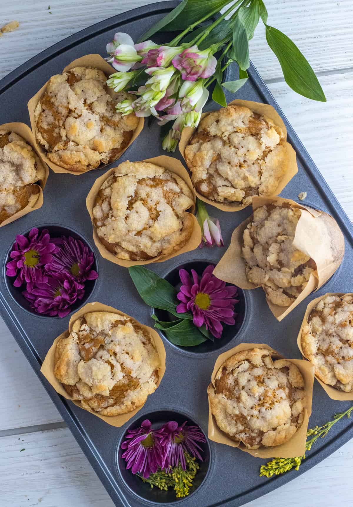 Pumpkin zucchini muffins in a muffin tin with purple flowers.