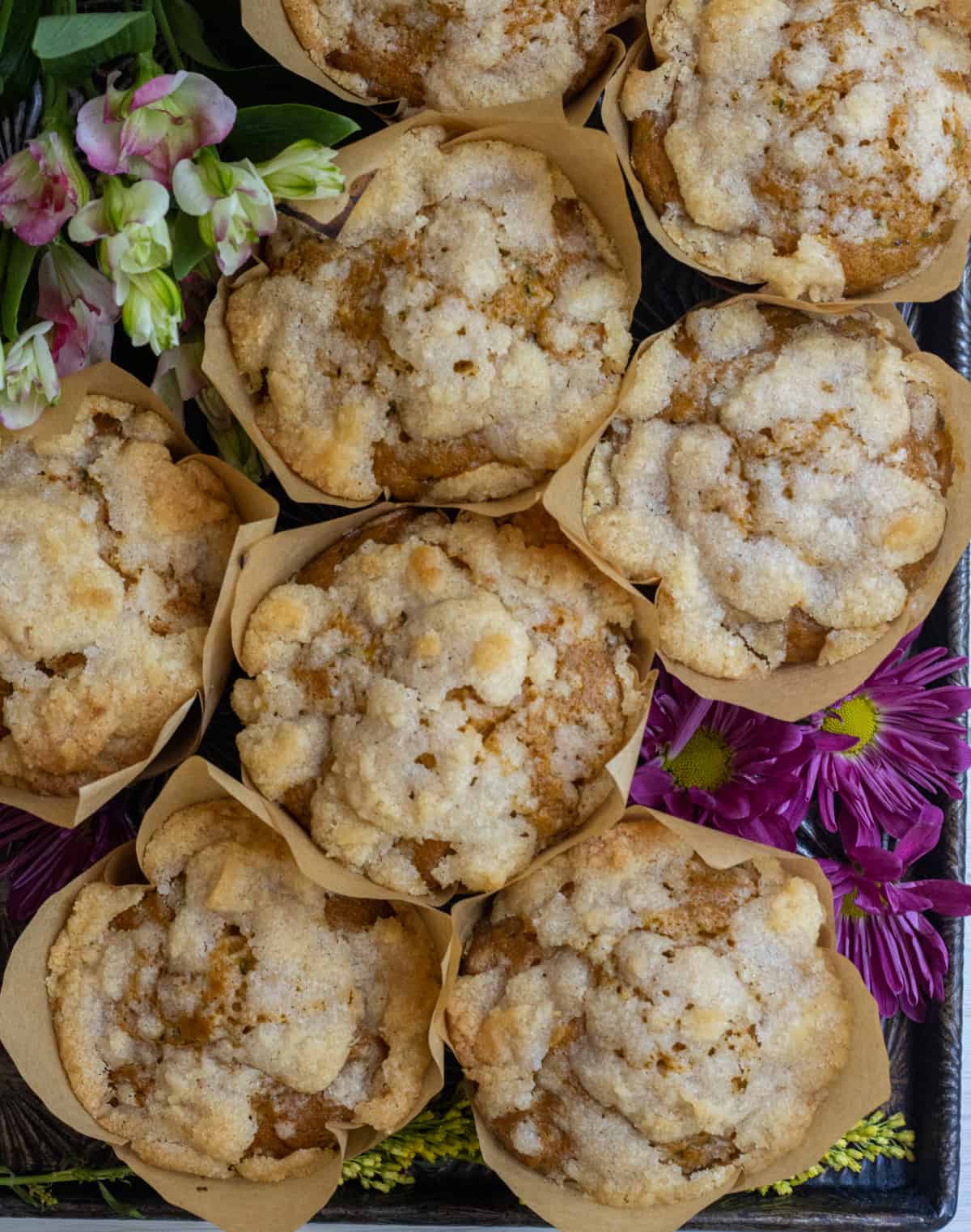 Streusel topped muffins on a tray with purple flowers.