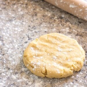 A pie dough disk on a floured counter next to a rolling pin.