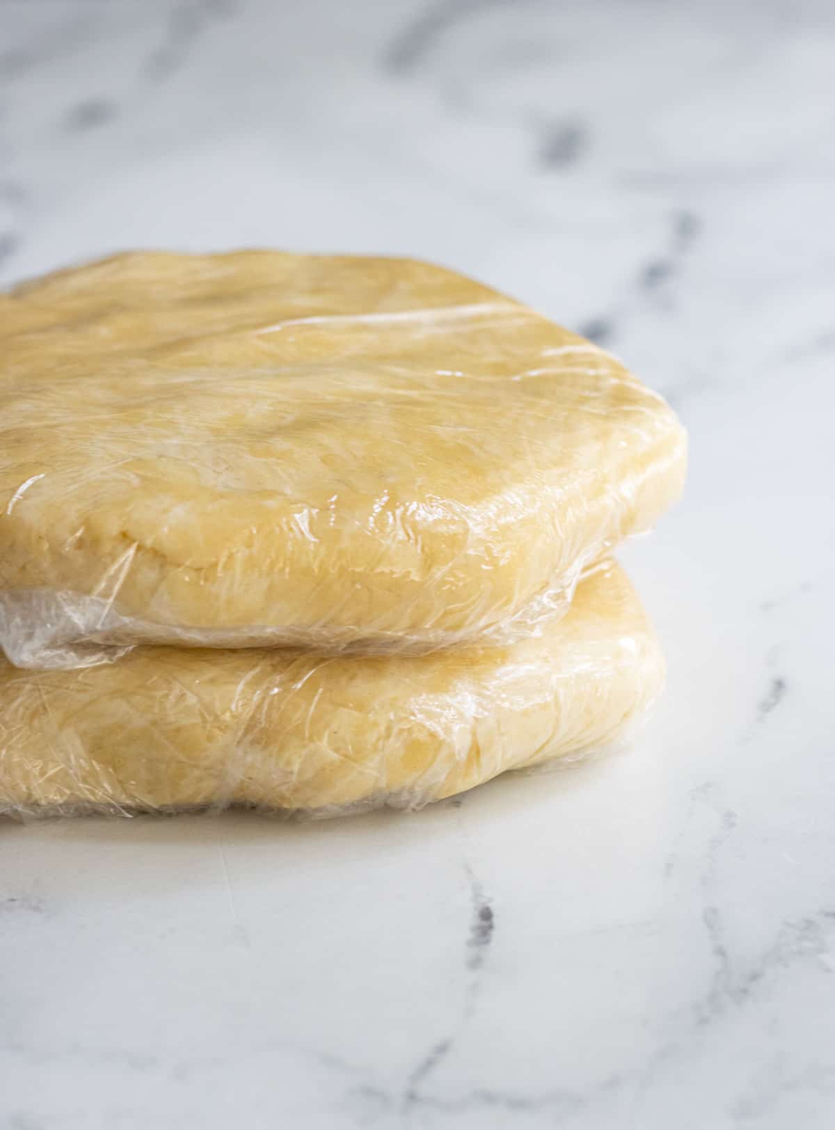 Two pie dough disks each wrapped in plastic.