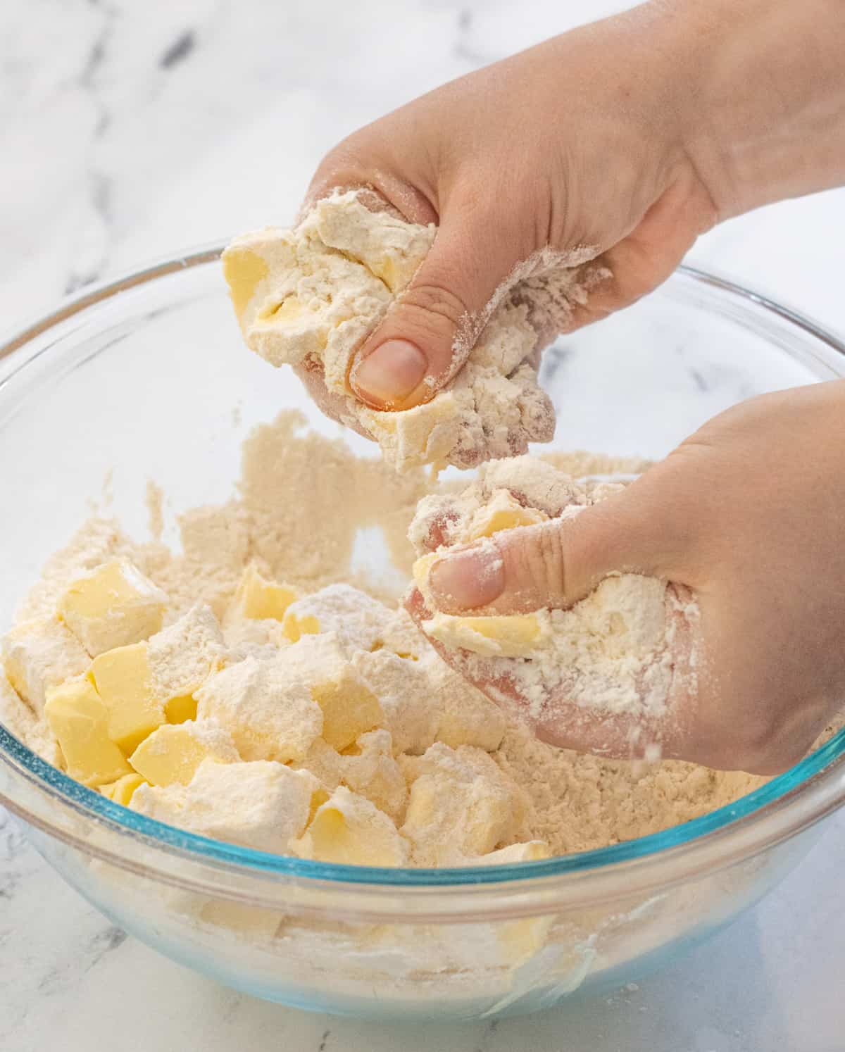 Two hands smashing butter into flour.