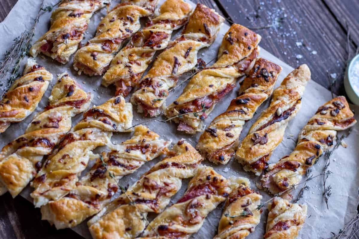 Ham and cheese puff pastry twists on parchment paper on a board with thyme sprigs and salt.