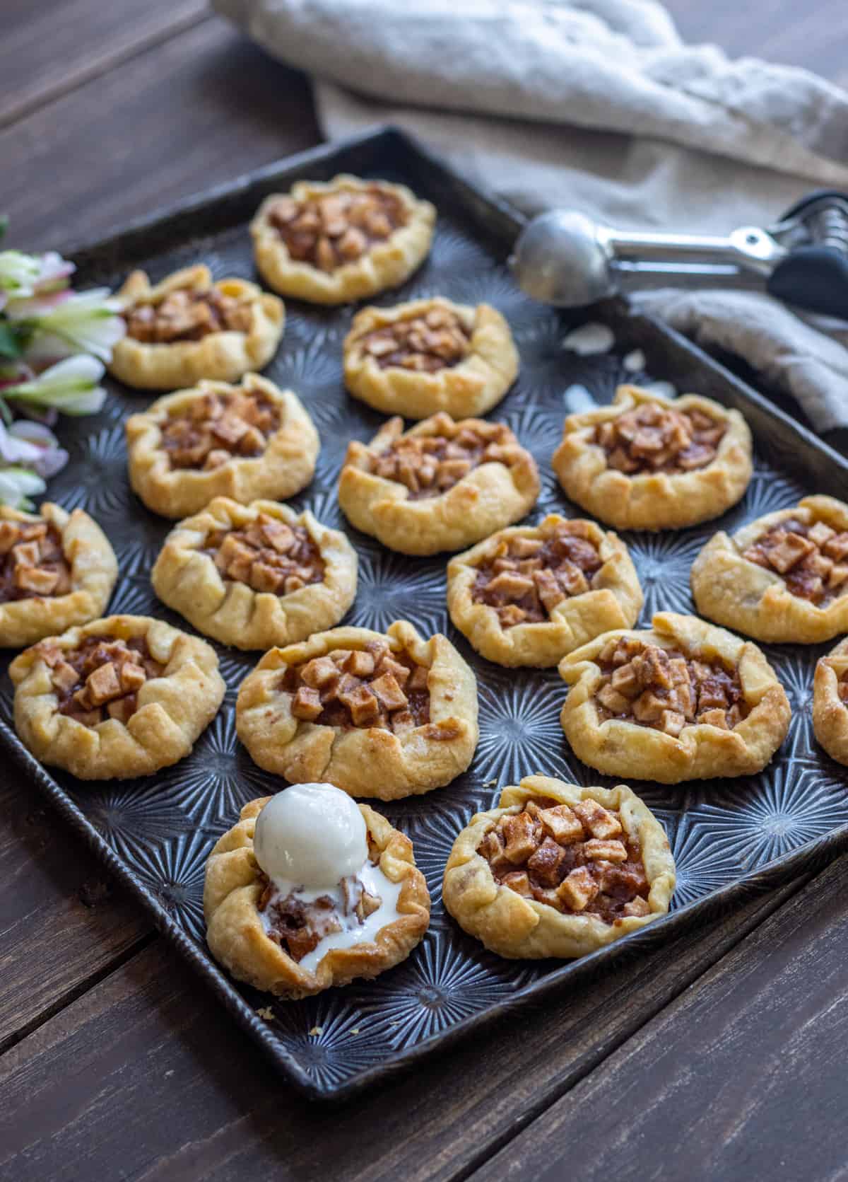 Mini apple galettes on a dark baking sheet with a scoop of vanilla ice cream on one.