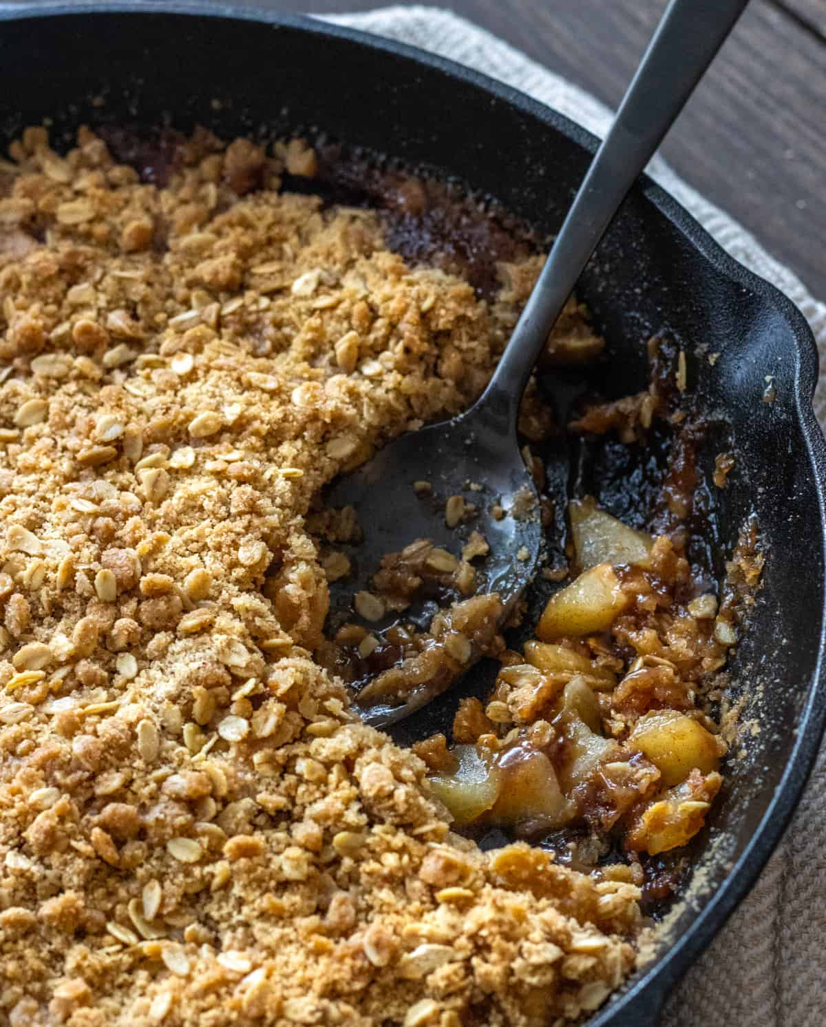 Apple crisp in a cast iron skillet with a large black spoon.