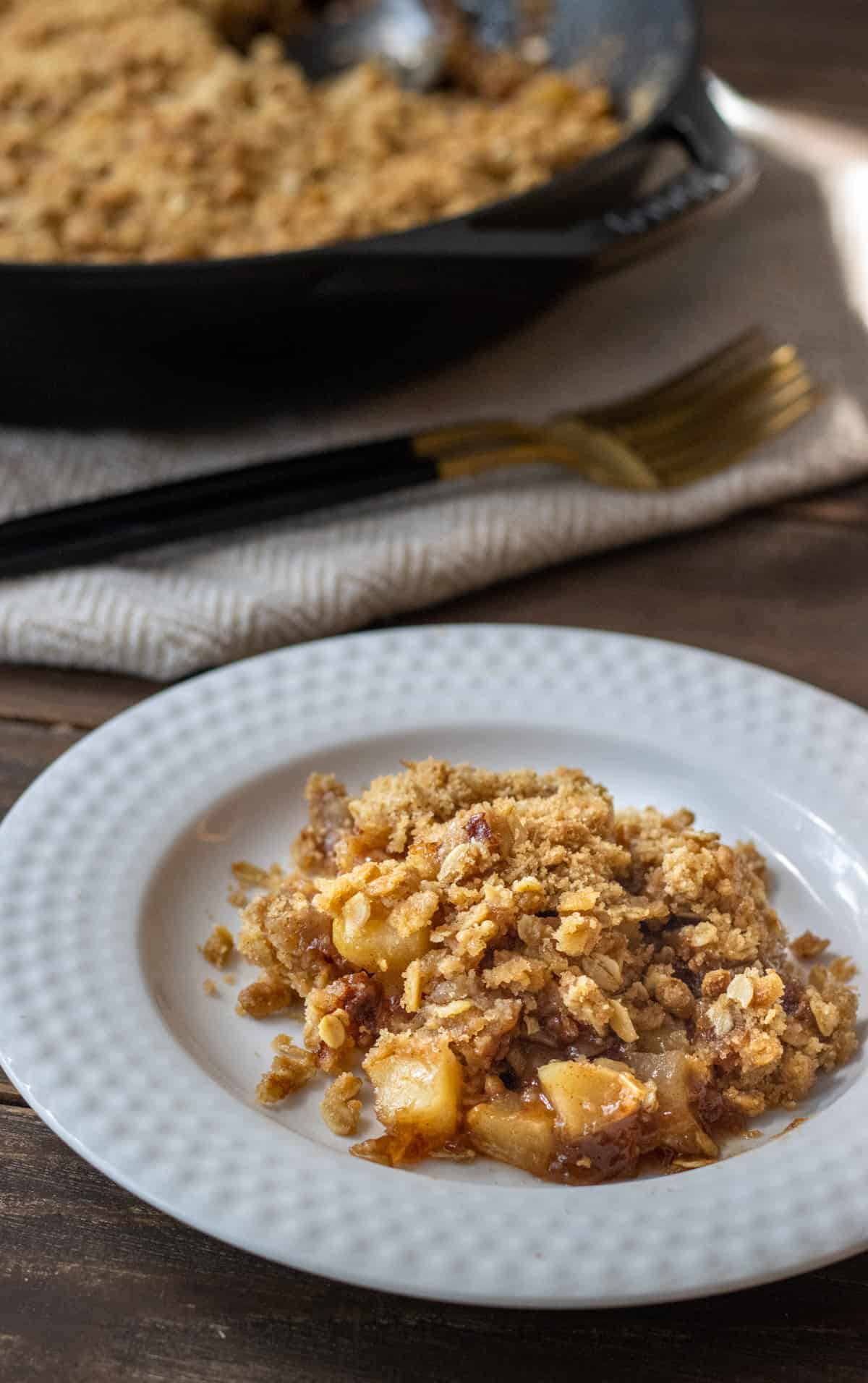 Plate with a scoop of apple crisp and the rest of the crisp in the background with two forks.