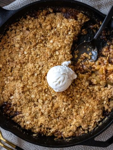 Apple Crisp in a cast iron skillet with a scoop of vanilla ice cream on top.
