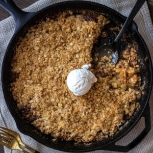 Apple crisp in a cast iron skilled with a scoop missing and ball of vanilla ice cream in the center.