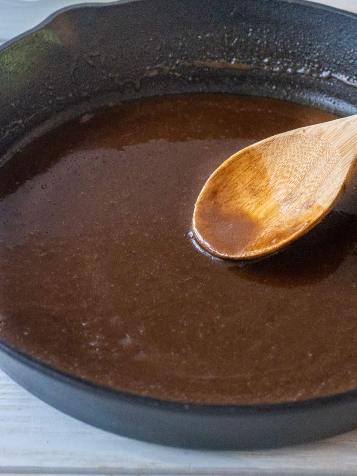 Brown sugar cinnamon sauce for the apples in a skillet with a wooden spoon.