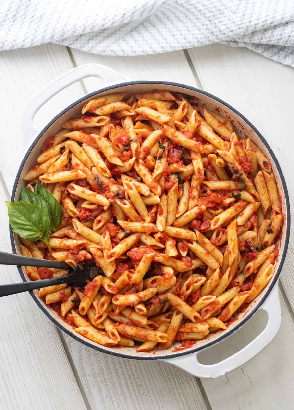 Penne pomodoro in a white casserole dish with basil leaves and spoons.