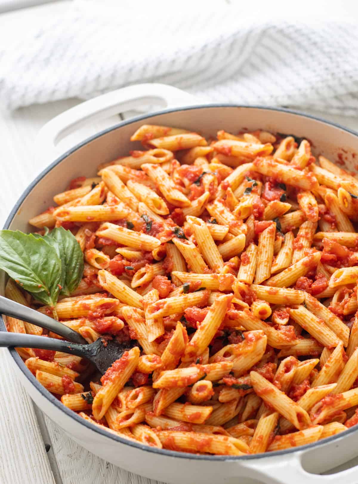 Penne pomodoro in a casserole dish with basil leaves and spoons.