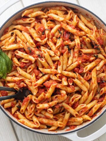 Pasta pomodoro in a large round casserole dish with basil leaves.