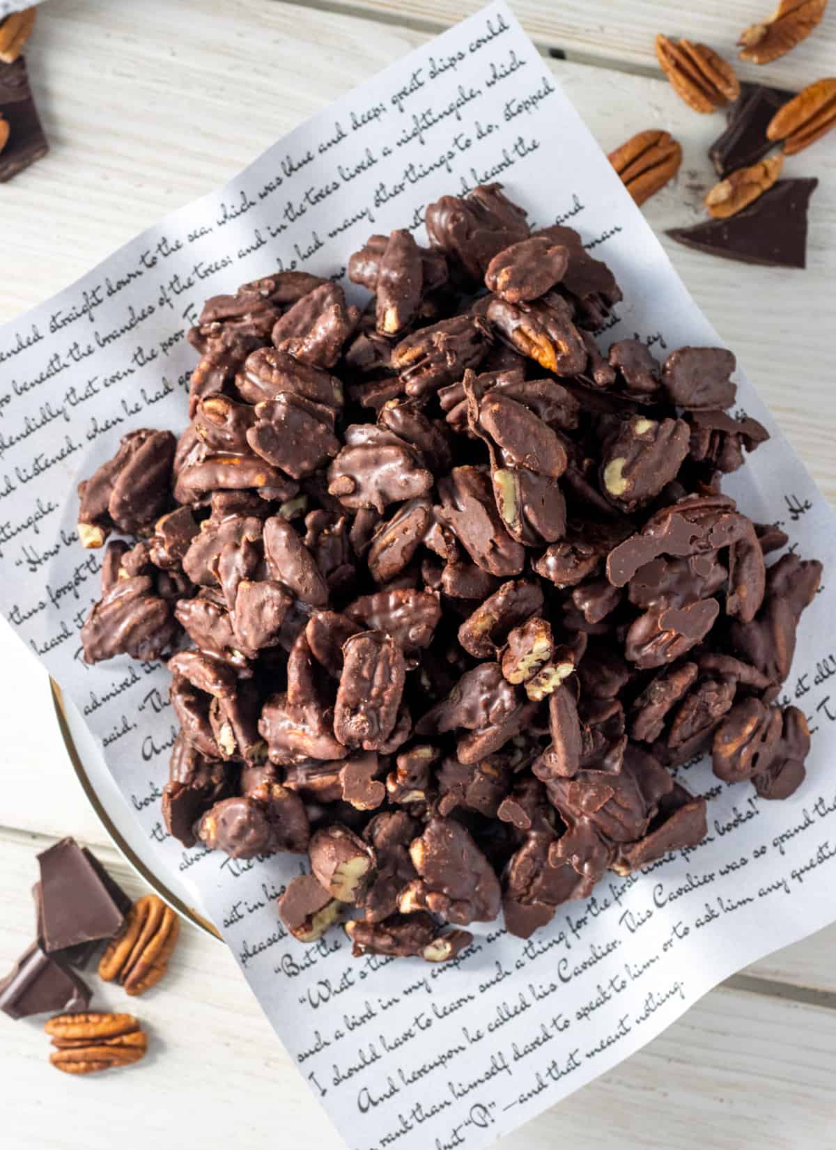 Chocolate covered pecans on a page from a book on a plate with chocolate and pecans all around.