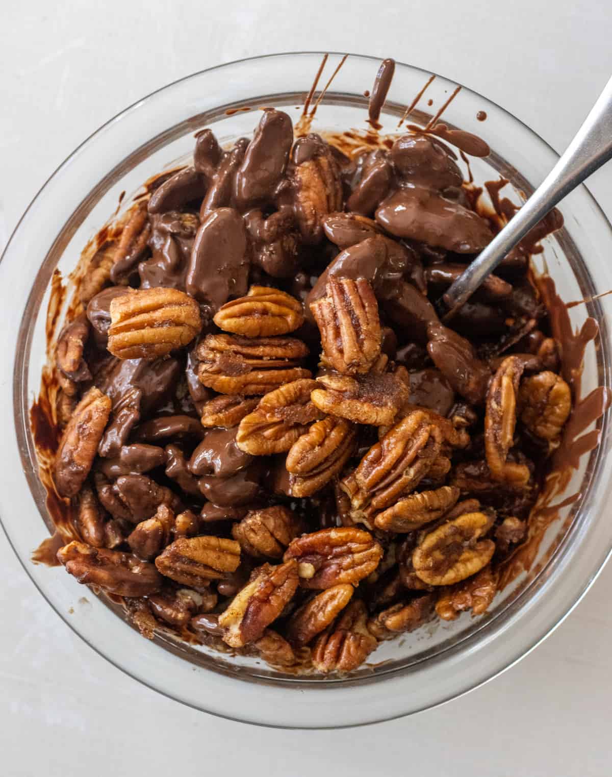Pecan halves tossed in melted chocolate in a bowl.