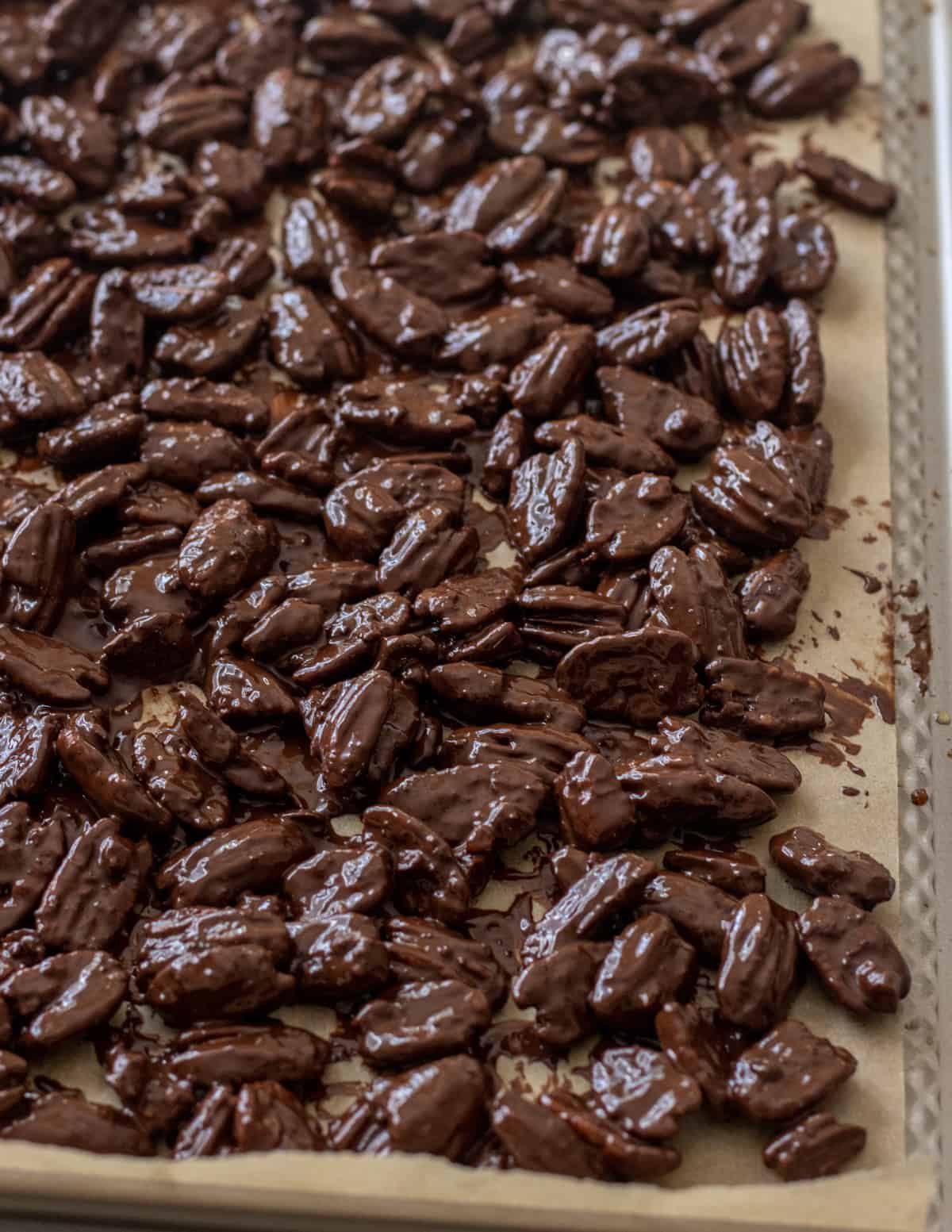 Chocolate covered pecans on a parchment lined baking sheet.