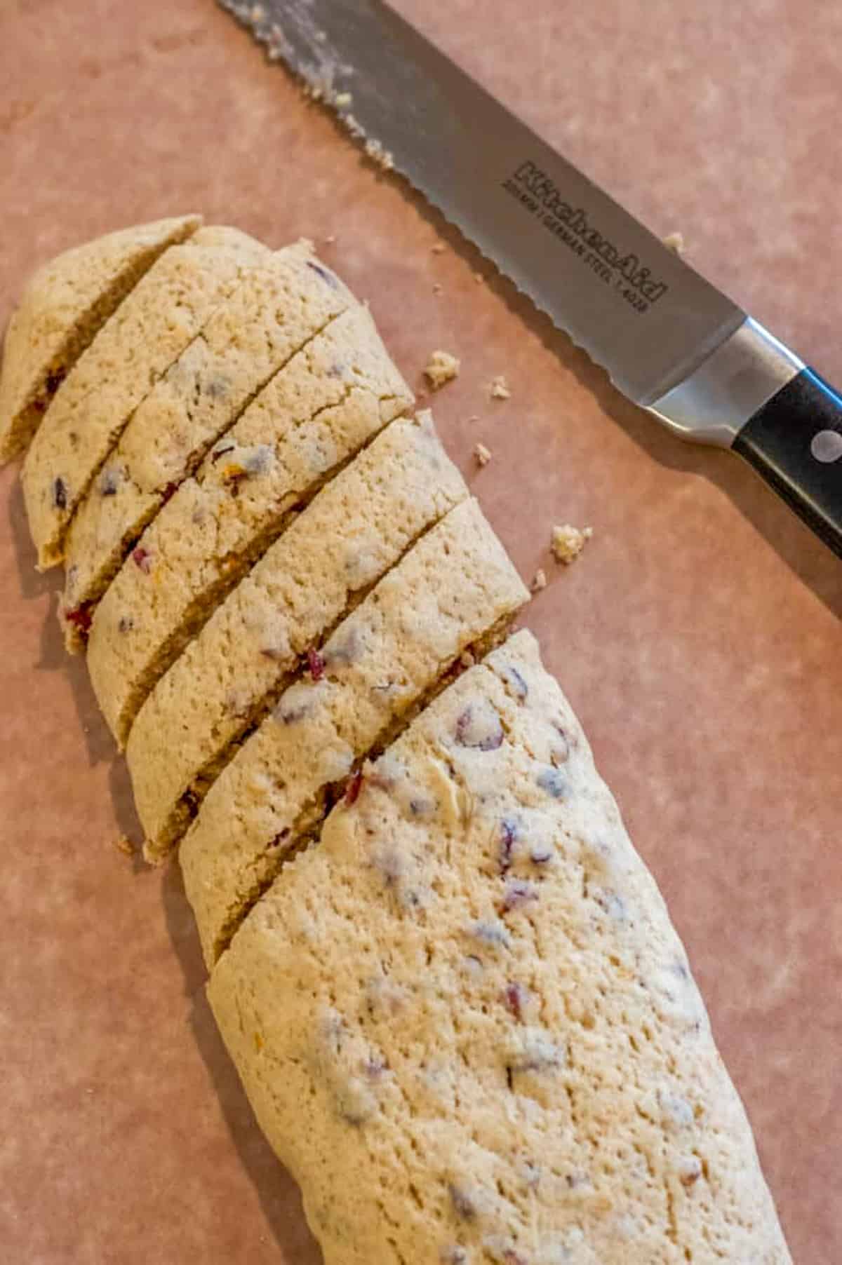 Baked biscotti log sliced into 1 inch thick cookies next to a serrated knife.