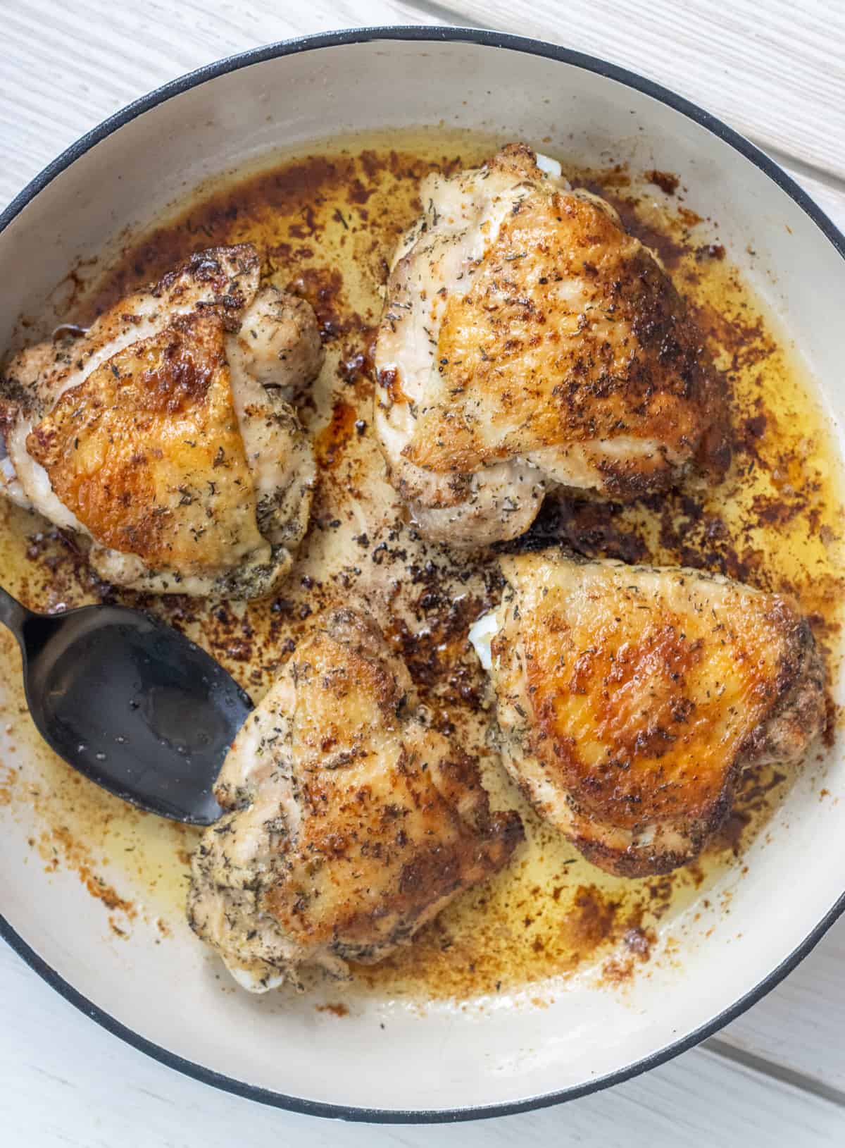 Four pan seared chicken thighs in the pan with a spoon.