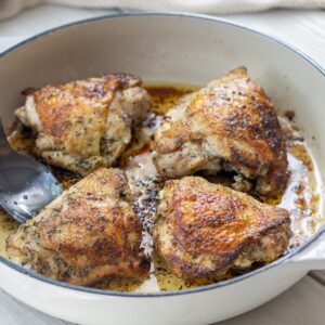 Four pan seared chicken thighs in the pan with a spoon.