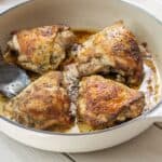 Four chicken thighs seared golden brown in a large skillet with a large spoon.