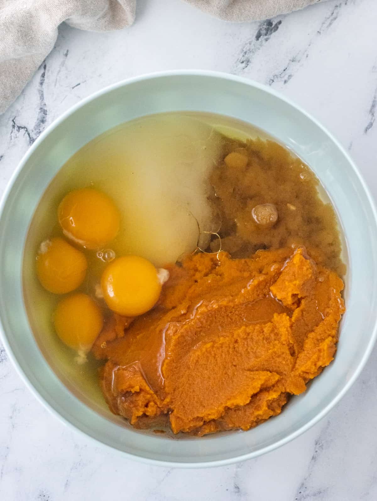 Sugar, brown sugar, pumpkin purée, four eggs, and oil in a bowl.