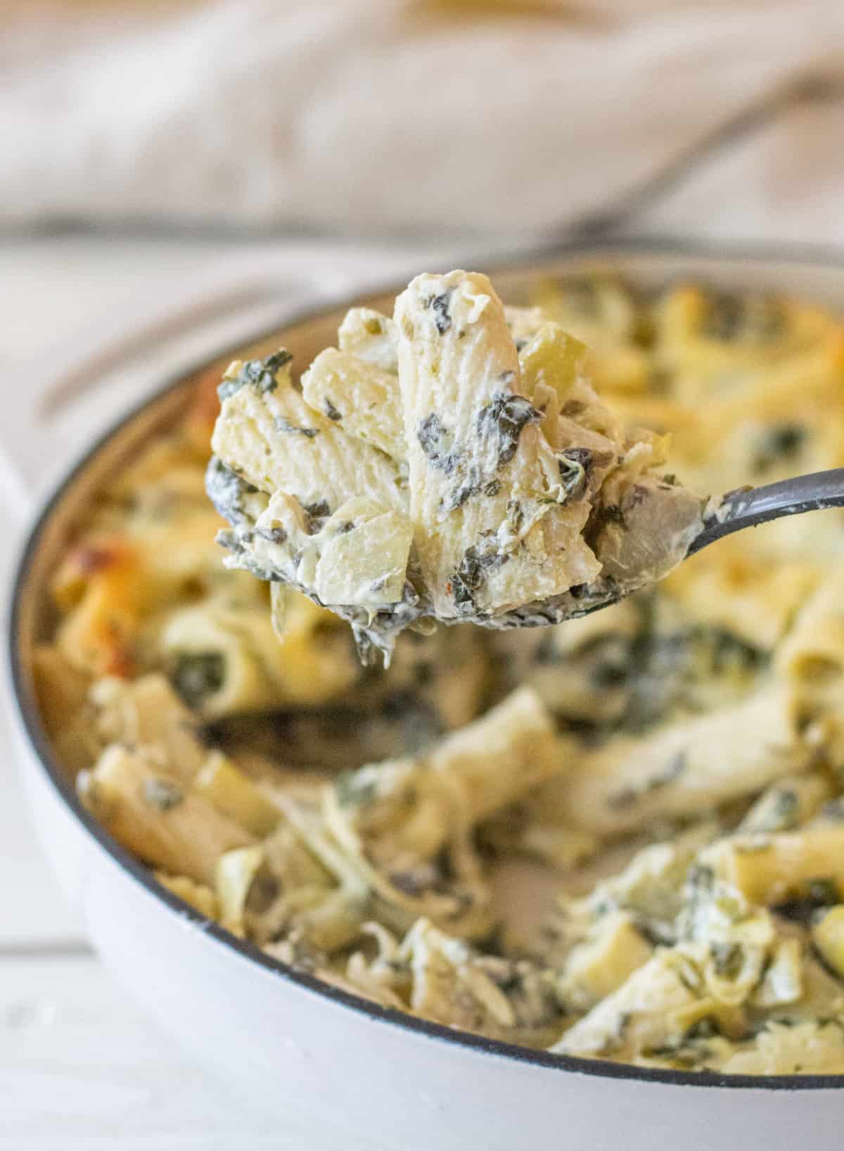 Forkful of rigatoni noodles in a spinach artichoke sauce.