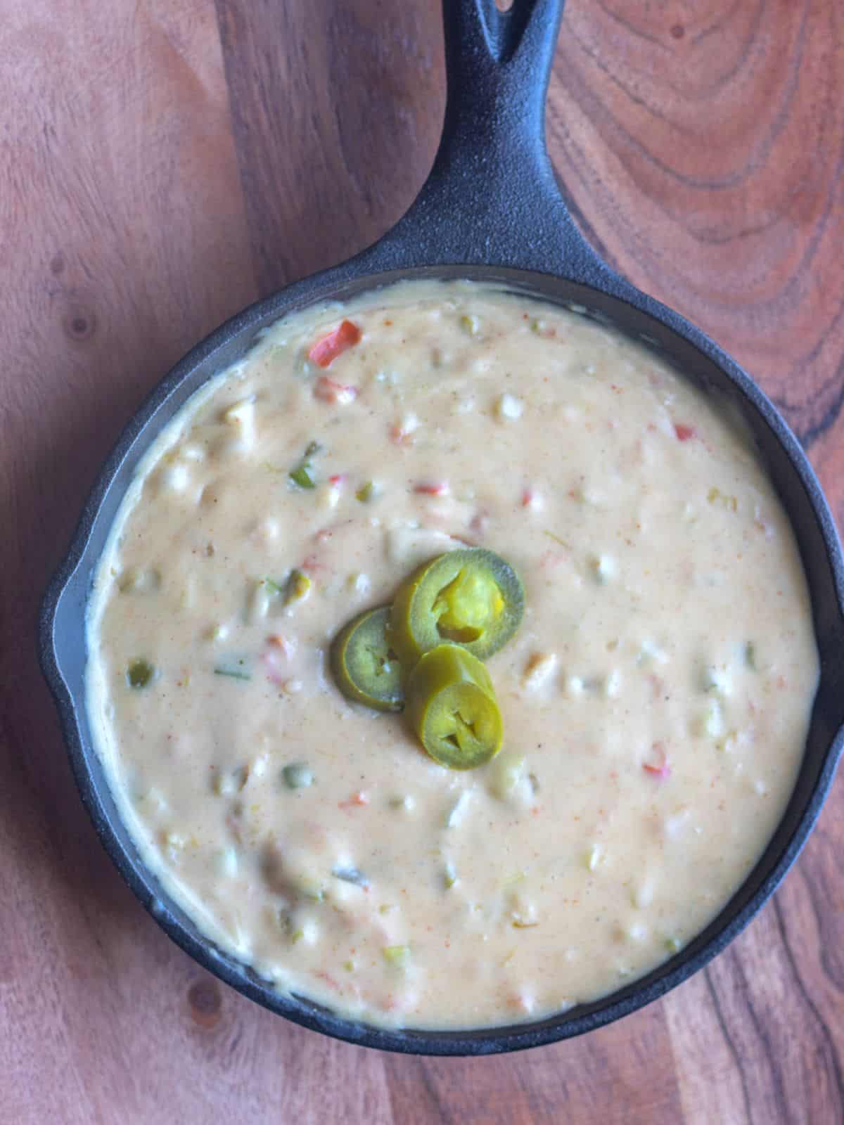 White queso dip in a cast iron skillet topped with jalapeño slices.