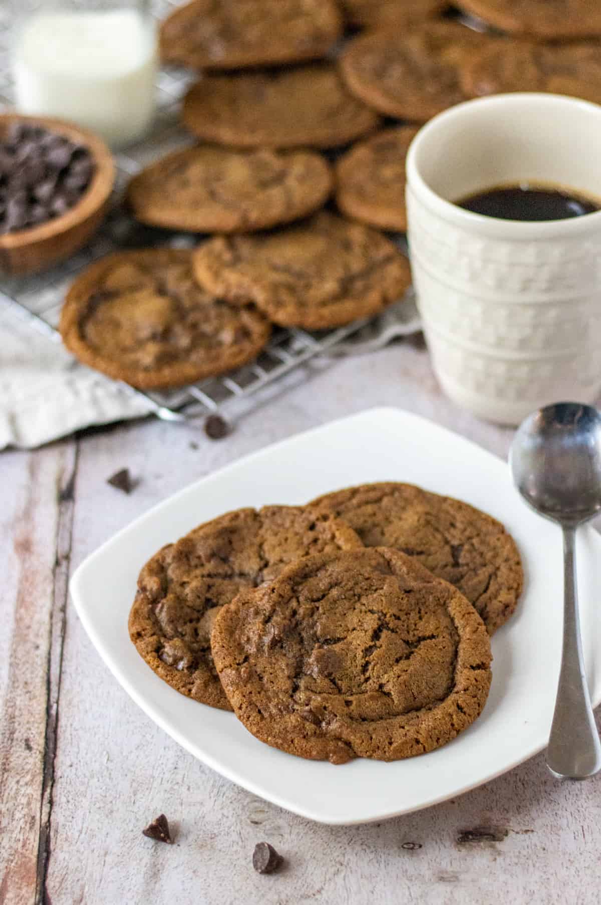 Coffee cookies on a plate next to a mug of coffee and more cookies in the back.