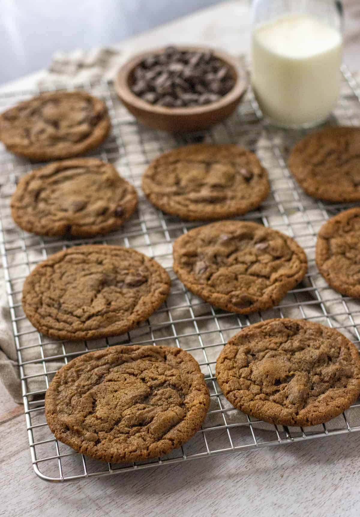 Coffee cookies on a wire rack with a bowl of chocolate chips and glass of milk.